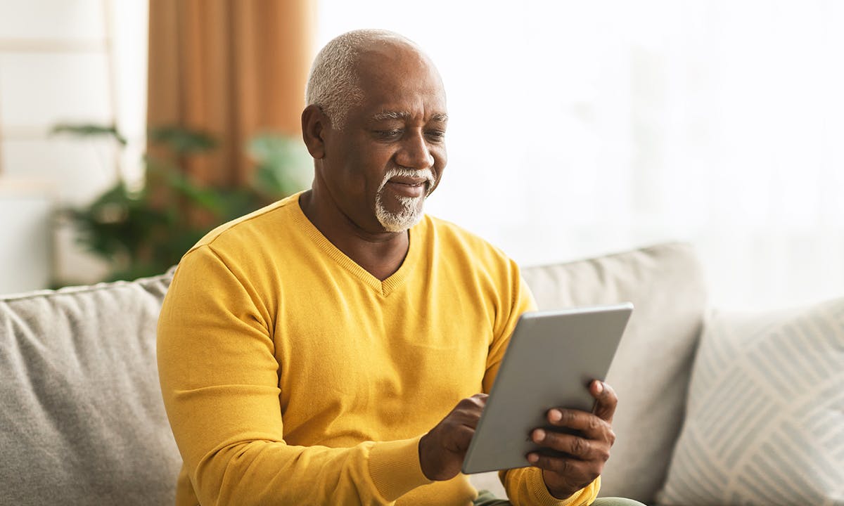 Older man in a yellow sweater using a tablet to complete the COPD population screener while sitting on a couch.