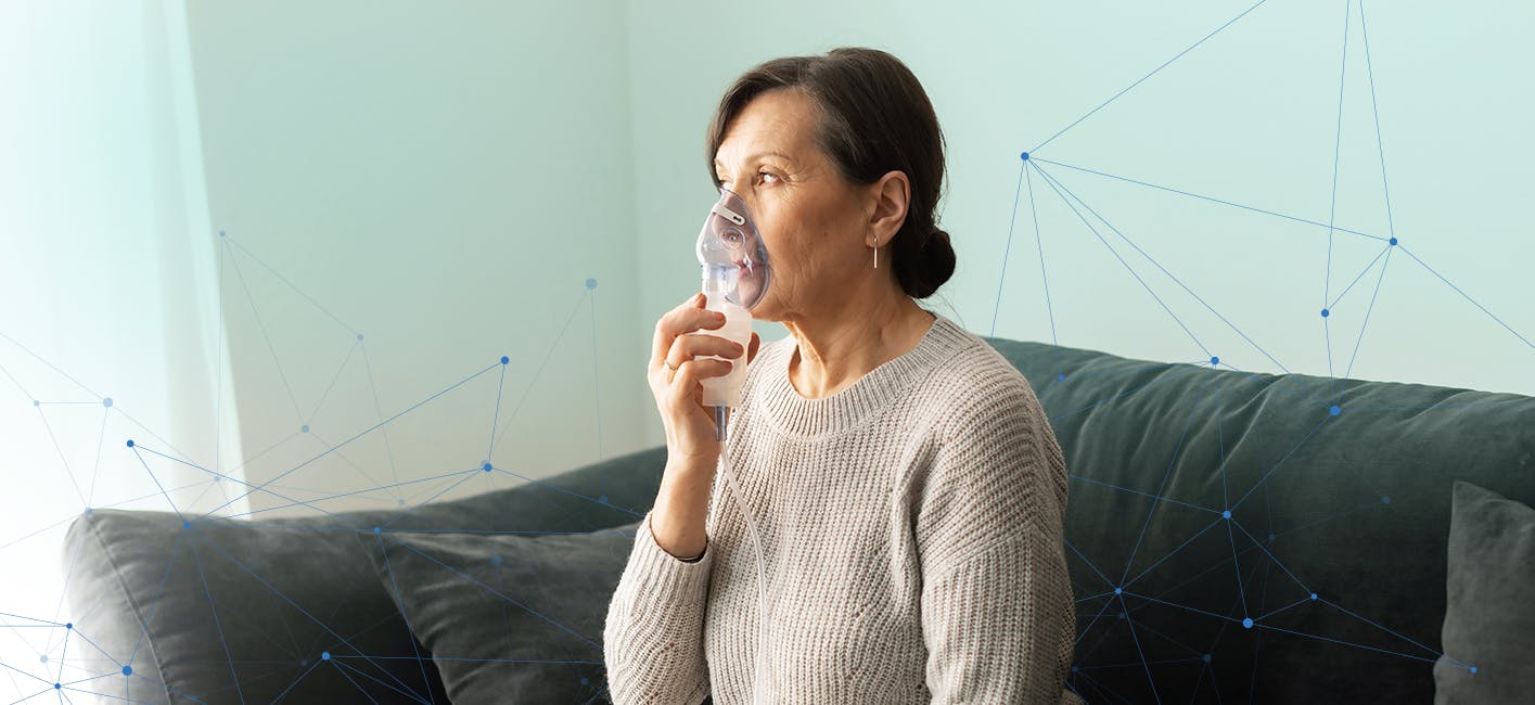 Middle-aged woman using nebulizer to manage COPD symptoms while seated on couch.